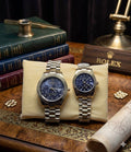 DUPE Rolex gold couples watch set with blue dials and metal bracelets, displayed on a cushion with classic decor